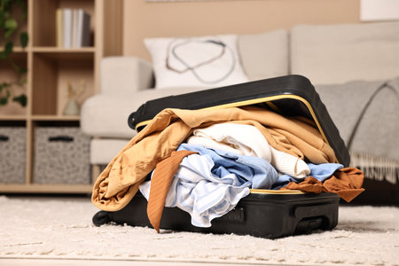 Open suitcase full of different messy clothes on floor indoors