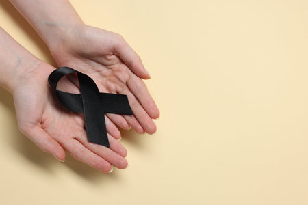 Woman with black ribbon on beige background, top view with space for text. Melanoma and mourning conceptの写真素材