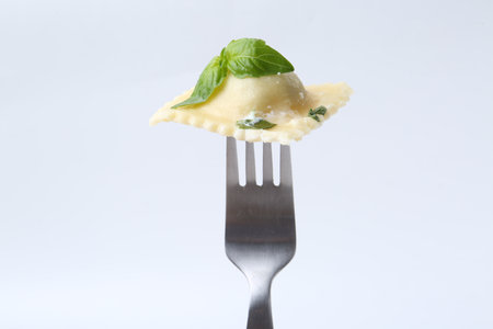 Delicious ravioli with cheese and basil on fork against white backgroundの写真素材