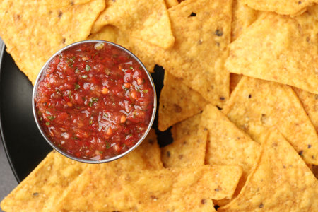 Delicious salsa sauce served with nachos on plate, top view