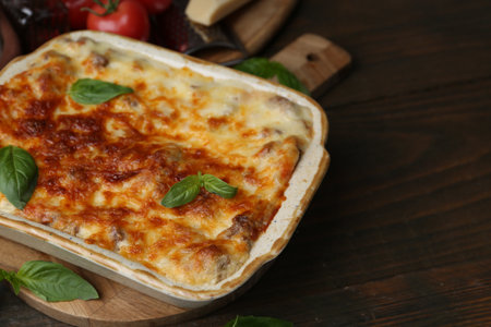 Delicious cooked lasagna in baking dish and basil on wooden table, closeup. Space for textの写真素材