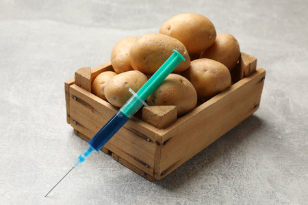 GMO concept. Potatoes and syringe with liquid in crate on gray textured table, closeupの写真素材