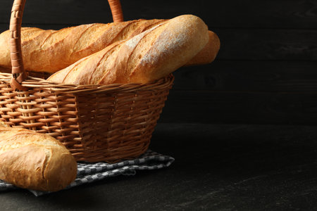 Wicker basket with fresh baguettes on black table, space for textの写真素材