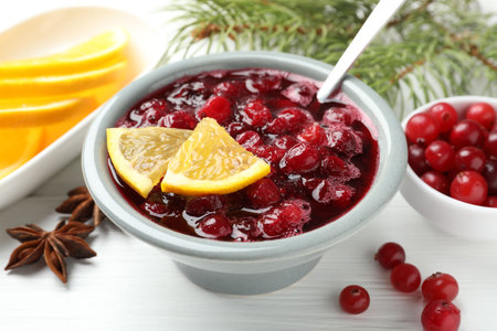 Tasty cranberry sauce in bowl, berries, orange, anise and fir tree branches on white wooden table, closeupの写真素材