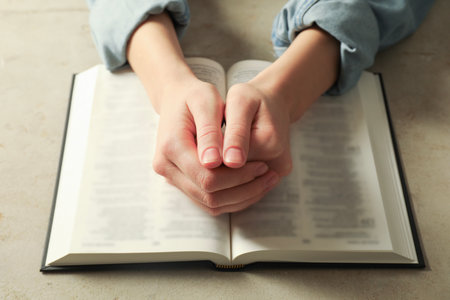 Woman with open Holy Bible in English language praying at beige table, closeup
