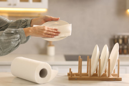 Woman wiping plate with paper towel at white marble table in kitchen, closeupの写真素材