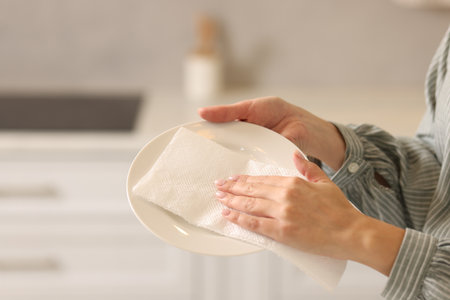 Woman wiping plate with paper towel in kitchen, closeupの写真素材