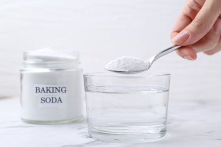 Woman adding baking soda to glass of water at white marble table, closeupの写真素材