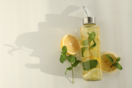 Lemon water with mint in bottle, fresh fruits and leaves on white table, flat lay. Space for textの写真素材