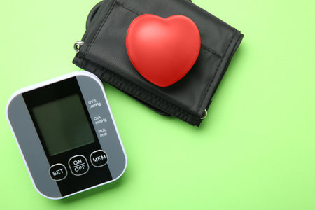 Blood pressure measuring device and squeeze heart on green background, top view