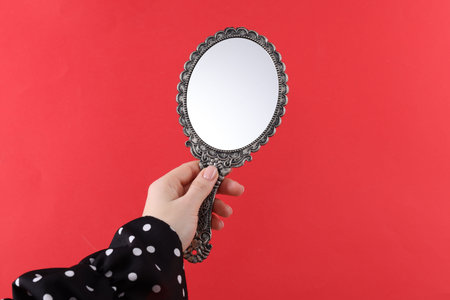 Woman holding beautiful mirror on red background, closeupの写真素材