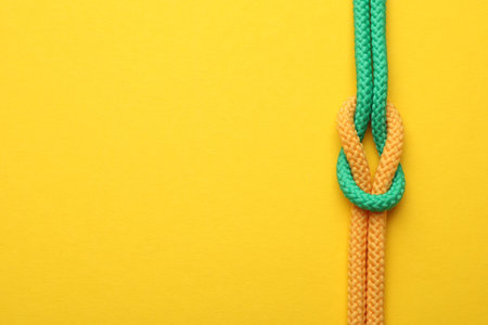 Colorful ropes tied in knot on yellow background, top view with space for text. Unity concept