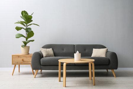 Comfortable sofa, tables and houseplant near gray wall in room