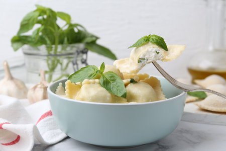 Taking delicious ravioli with cheese and basil from bowl at table, closeupの写真素材