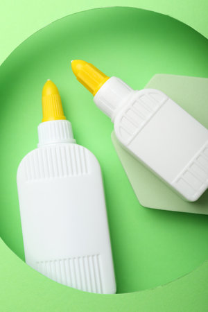 Bottles of glue on light green background, top view