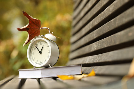 Autumn time. Alarm clock and book on bench in park, closeupの写真素材