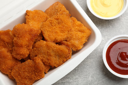 Delicious chicken nuggets in takeaway container with sauces on gray textured table, flat layの写真素材