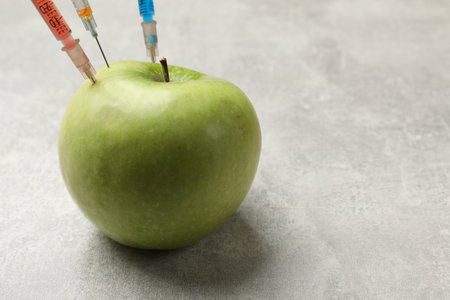 GMO concept. Green apple with different syringes on gray textured table, closeup. Space for textの写真素材