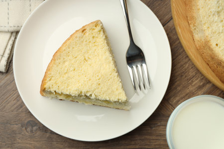 Piece of delicious sponge cake served on wooden table, flat lay