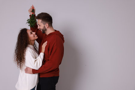 Lovely couple under mistletoe bunch on light grey background. Space for textの写真素材