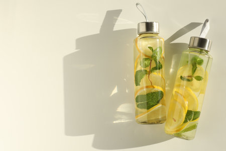 Lemon water with mint in bottles, fresh fruits and leaves on white table, top view. Space for textの写真素材