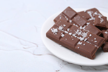 Pieces of chocolate with salt on white table, closeup. Space for textの写真素材