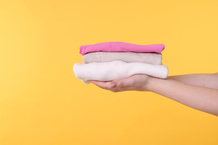 Woman holding stacked clothes on yellow background, closeup. Space for textの写真素材