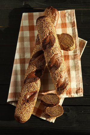 Fresh baguettes with sesame on black wooden table, flat lay