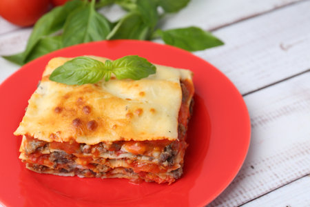 Piece of delicious cooked lasagna with basil on light wooden table, closeupの写真素材