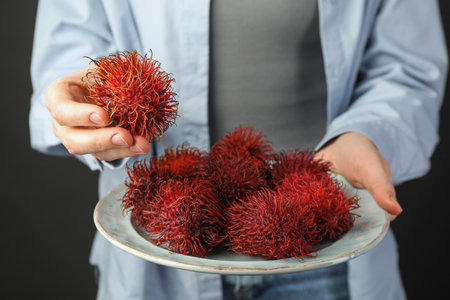 Woman holding fresh rambutans on plate against black background, closeupの写真素材