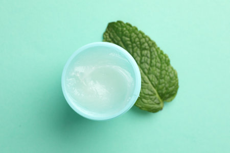 Natural lip balm and mint leaf on turquoise background, top viewの写真素材