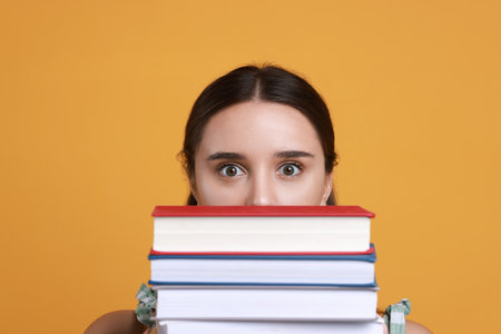 Person with stack of books before exam on orange background, closeupの写真素材