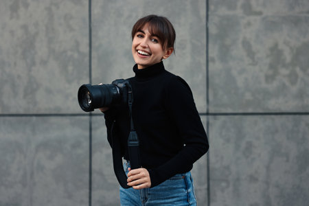 Professional photographer with digital camera near grey wall outdoors
