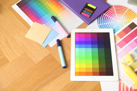Designer's workplace with tablet, palettes and stationery on wooden table, above view