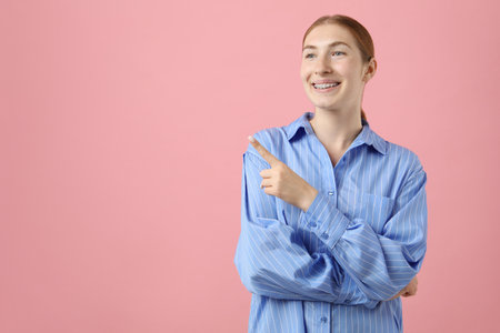 Smiling girl with braces on pink background, space for textの写真素材