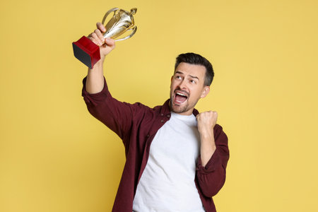 Happy winner with golden trophy cup on yellow backgroundの写真素材