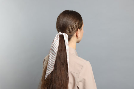 Teenage girl with stylish hair clips and bandana on light gray background, back viewの写真素材