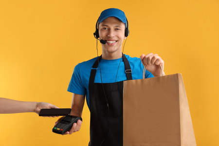 Fast-food worker taking payment from client via terminal on orange background, closeupの写真素材