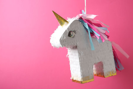 Bright pinata in shape of unicorn hanging on pink background