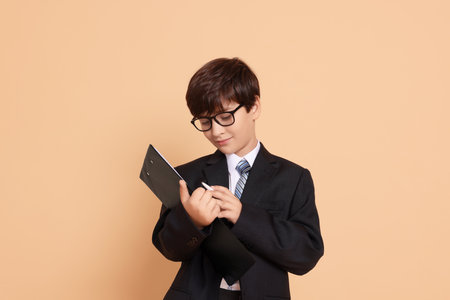 Boy with clipboard pretending to be accountant on beige background. Dreaming of future professionの写真素材