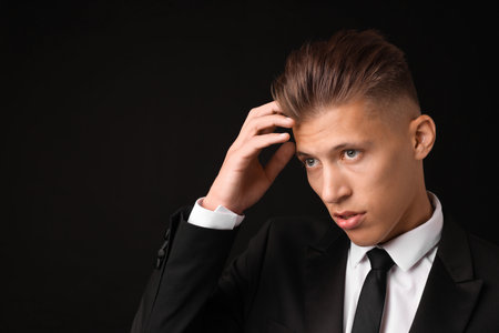 Confident young man with stylish haircut on black background. Space for textの写真素材