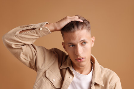 Confident young man with stylish haircut on brown backgroundの写真素材