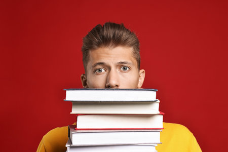 Emotional student with stack of books having stress before exam on red backgroundの写真素材