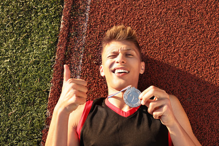 Happy winner with silver medal showing thumbs up at stadiumの写真素材