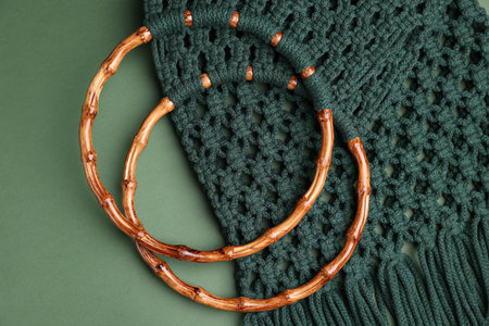 Macrame shopping bag with wooden handles on green background, top view