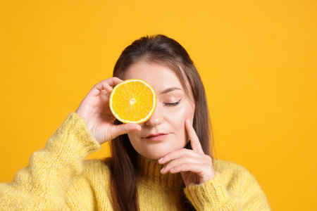 Person holding orange half near eye on orange background