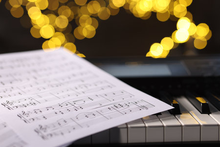 Sheet with musical notes on piano against blurred lights, closeup. Bokeh effectの写真素材