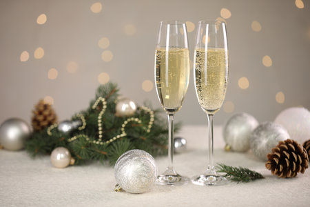 Delicious champagne in glasses and Christmas decor on white table against blurred lights, space for textの写真素材