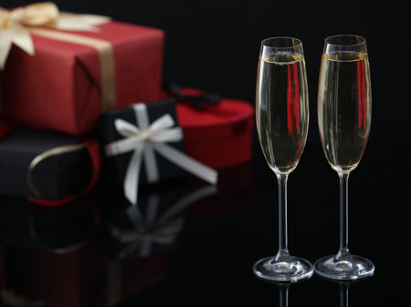 Delicious champagne in glasses and Christmas presents on black mirror surface, closeup. Space for textの写真素材