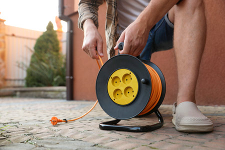 Man with extension cord reel in backyard, closeup. Space for textの写真素材
